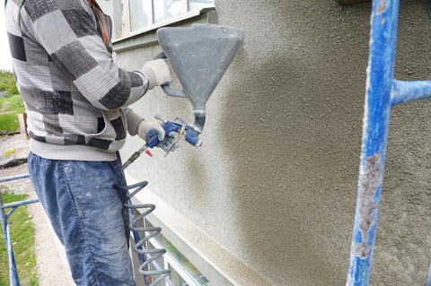 A building contractor is rendering, plastering, coating the exterior wall of a building using plaster sprayer machine, stucco concrete sprayer gun.