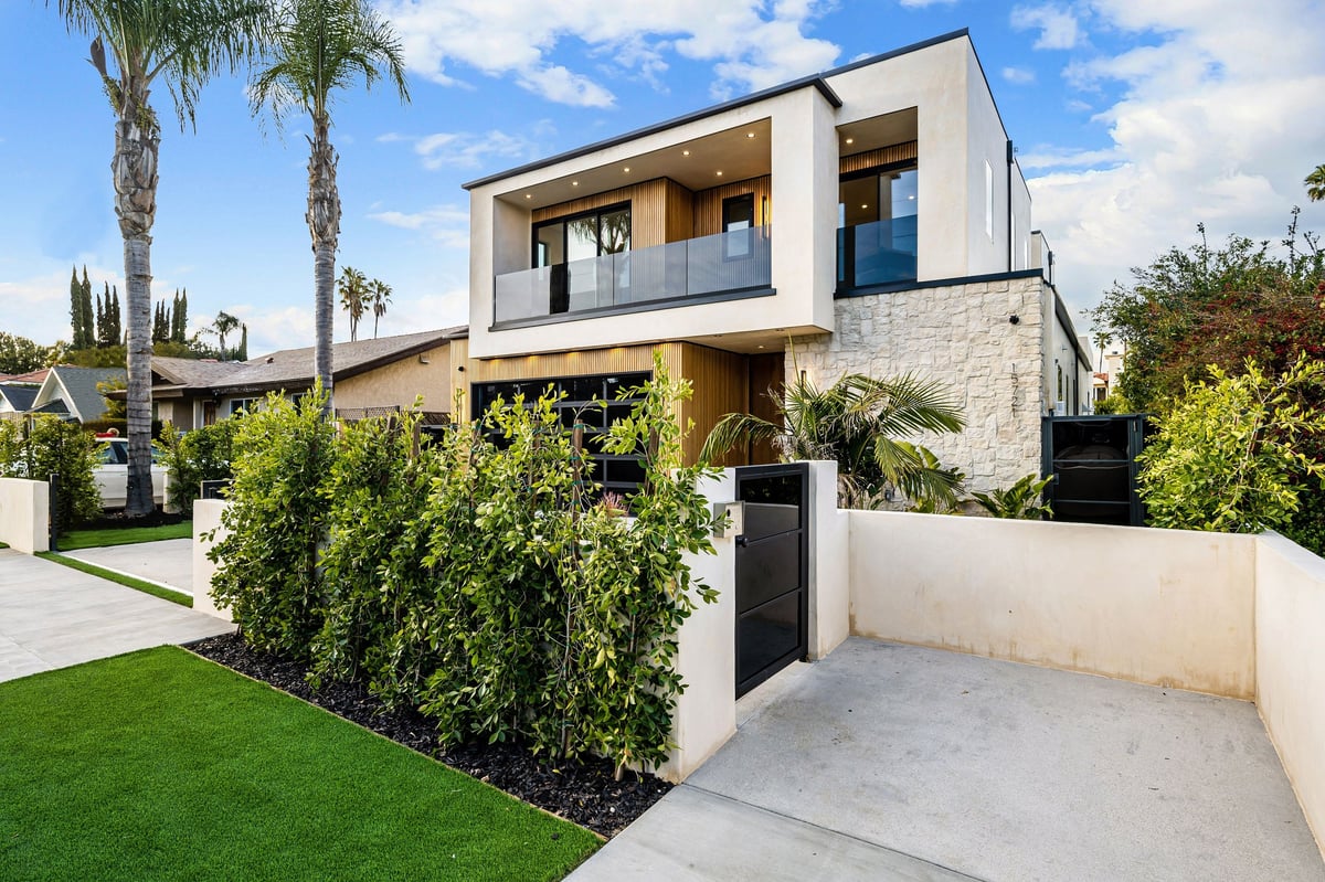 Modern two-story house with a clean and minimalist design, featuring a front yard with lush greenery and palm trees under a blue sky.