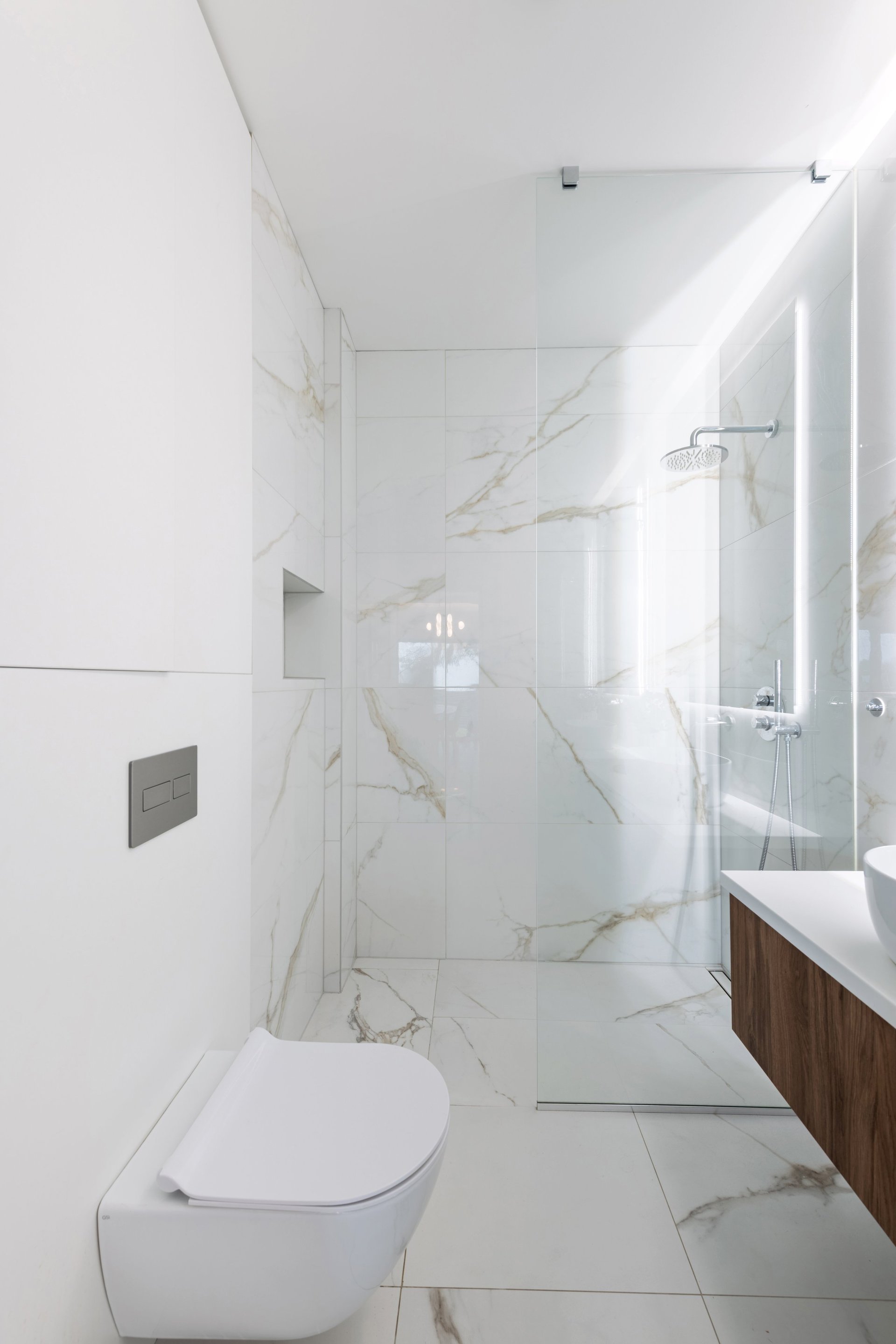 Bright modern bathroom with frameless walk-in glass shower, marble-look tile and a floating vanity