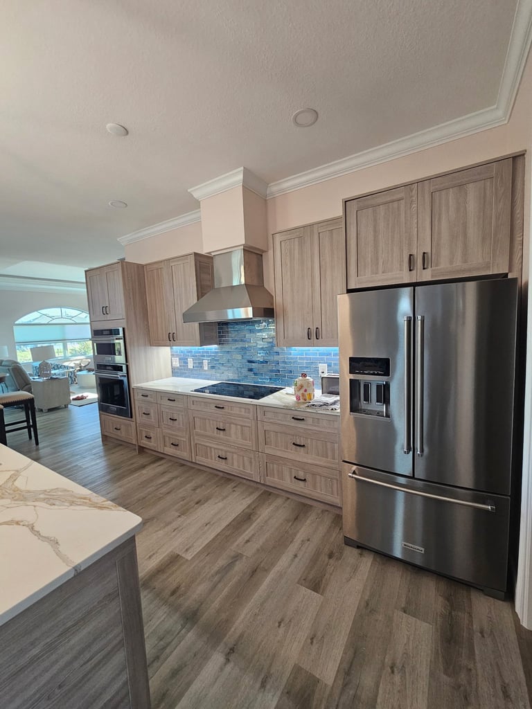 Bradenton Beach kitchen showing a stainless steel French-door refrigerator, light wood-grain cabinets and wood-look plank flooring.