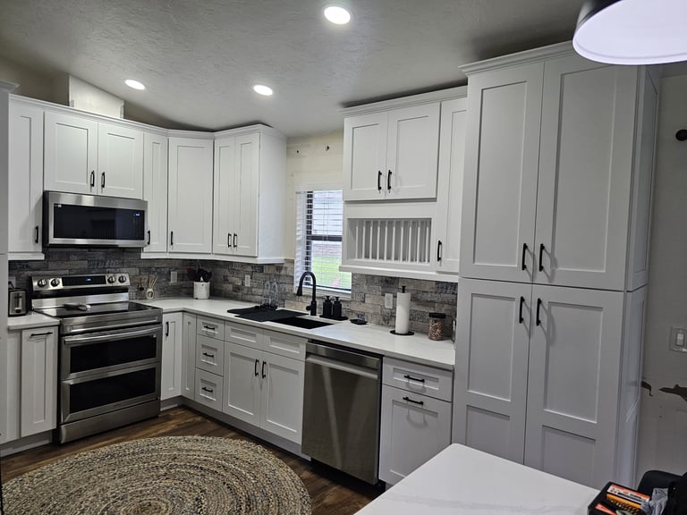 White shaker kitchen cabinets with dark hardware, stainless steel range, hood and refrigerator.