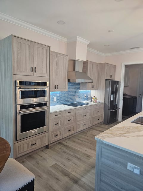 Wood-grain kitchen cabinetry with built-in appliances, stainless steel range hood and blue tile backsplash.