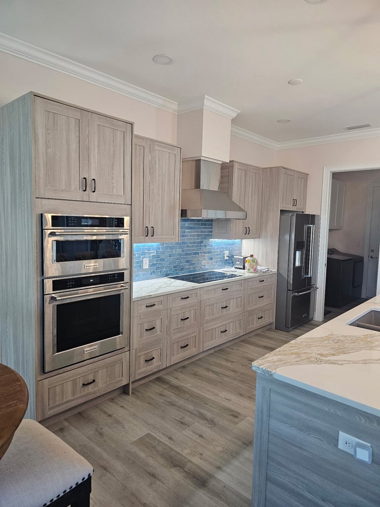 Wood-grain kitchen cabinetry with built-in stainless steel appliances, a range hood and a blue tile backsplash.