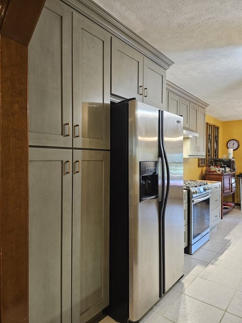 Tall gray shaker cabinetry surrounding a stainless steel refrigerator.