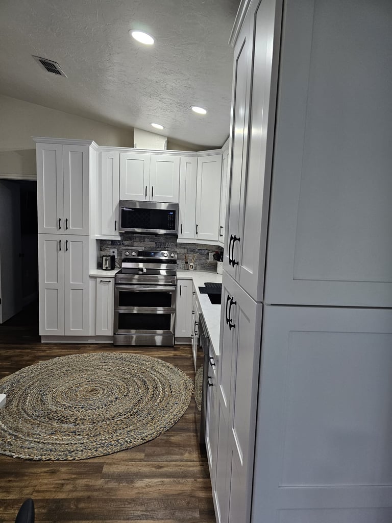 White shaker kitchen cabinets with dark hardware, veined countertops and glass-front upper cabinets.