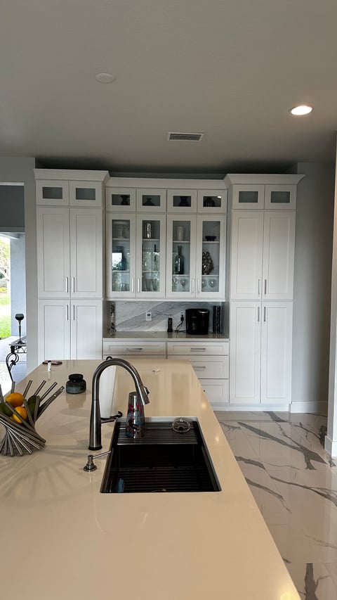 White kitchen storage wall with glass-front display cabinets, drawers and a coffee station.