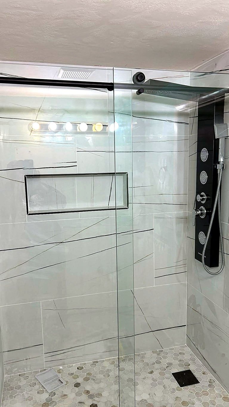 Venice shower with veined white wall tile, wide recessed niche, hexagonal floor and sliding glass doors.