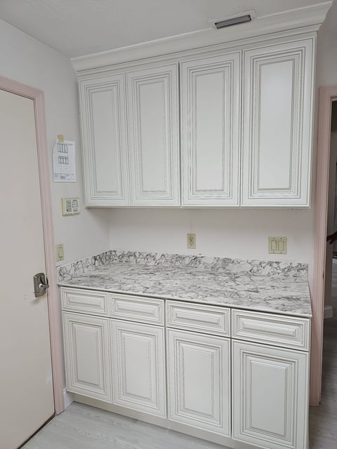 Laundry room storage wall with light raised-panel cabinets and gray-veined countertop.