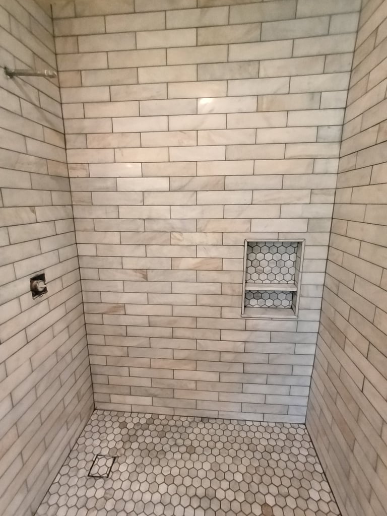 Detail of a recessed shower niche with hexagonal tile backing and shelf in a Sarasota shower remodel.