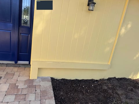 After: Yellow-painted vertical entry paneling and lower trim beside the dark blue front door.