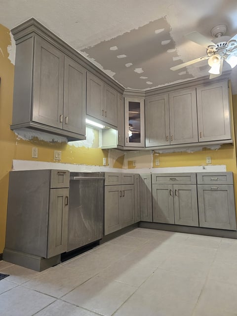 Gray kitchen cabinetry installation with corner cabinets and dishwasher area during renovation.