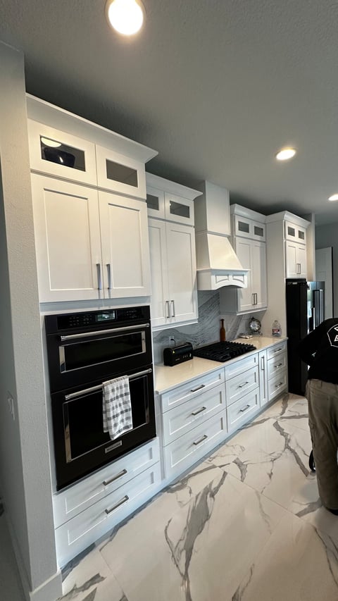 Built-in kitchen appliances beside white cabinetry, cooktop and decorative range hood.