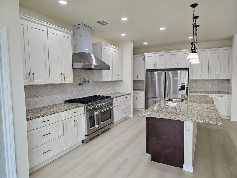 Kitchen remodel with white cabinetry, stainless steel range hood, patterned backsplash and center island.
