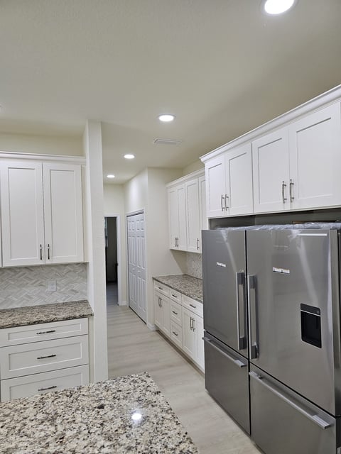 White kitchen storage cabinetry with stainless steel refrigerator and light countertops.