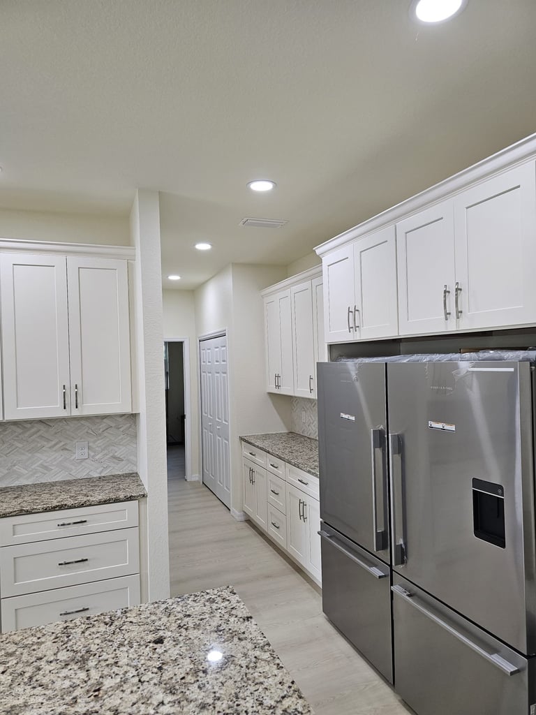 White kitchen storage cabinetry with stainless steel refrigerator and light countertops.