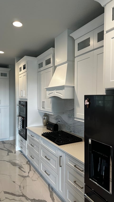 Decorative white kitchen range hood with shaker cabinetry and a gray-veined backsplash.