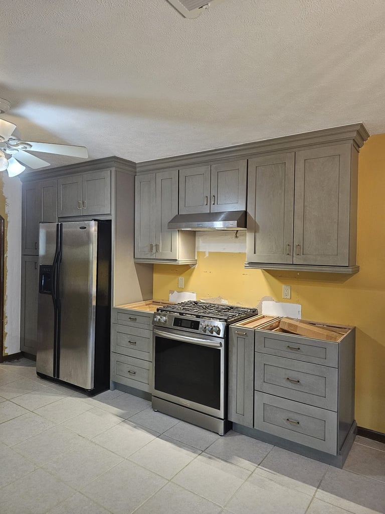 Kitchen renovation in progress with gray shaker cabinets, stainless steel refrigerator and range.