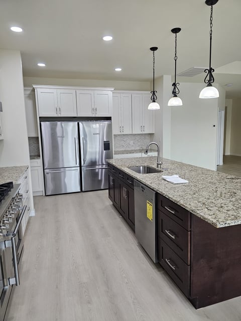 Kitchen with dark island cabinetry, white perimeter cabinets and stainless steel refrigerator.