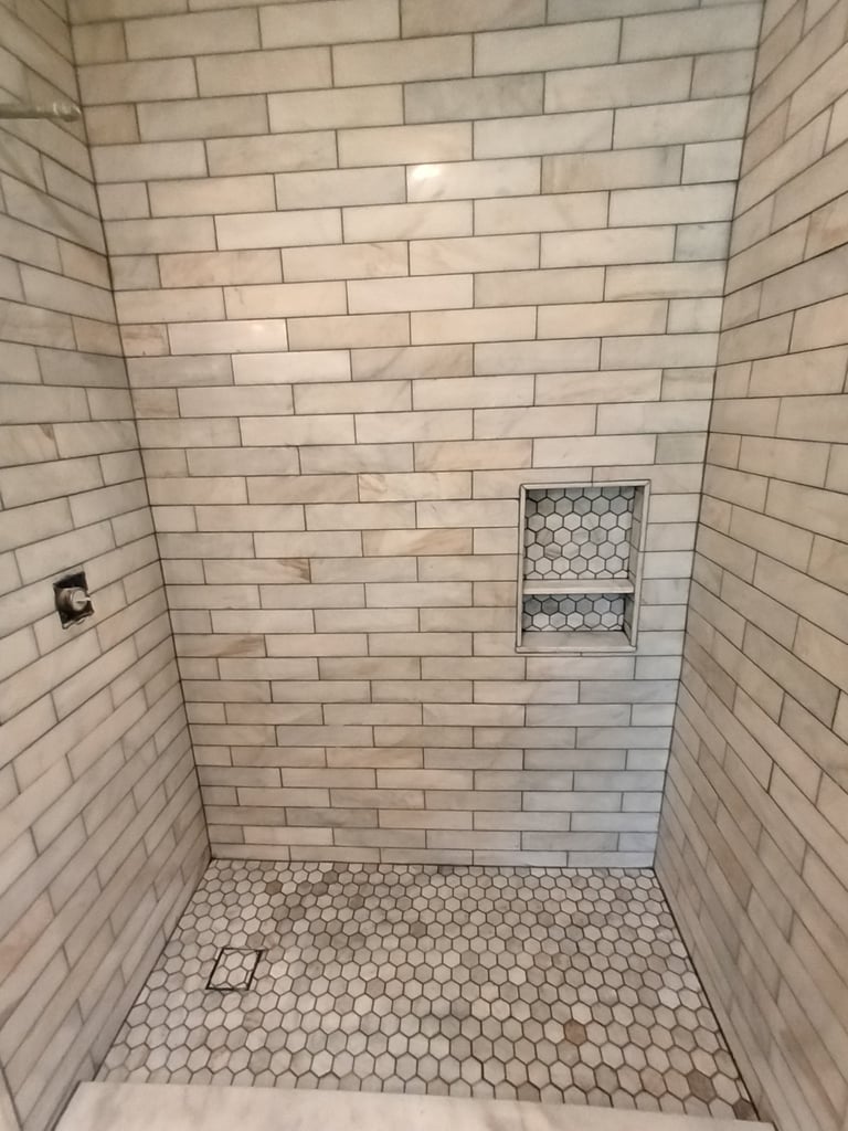 Sarasota shower tilework with marble-look wall tiles, hexagonal mosaic floor and recessed storage niche.