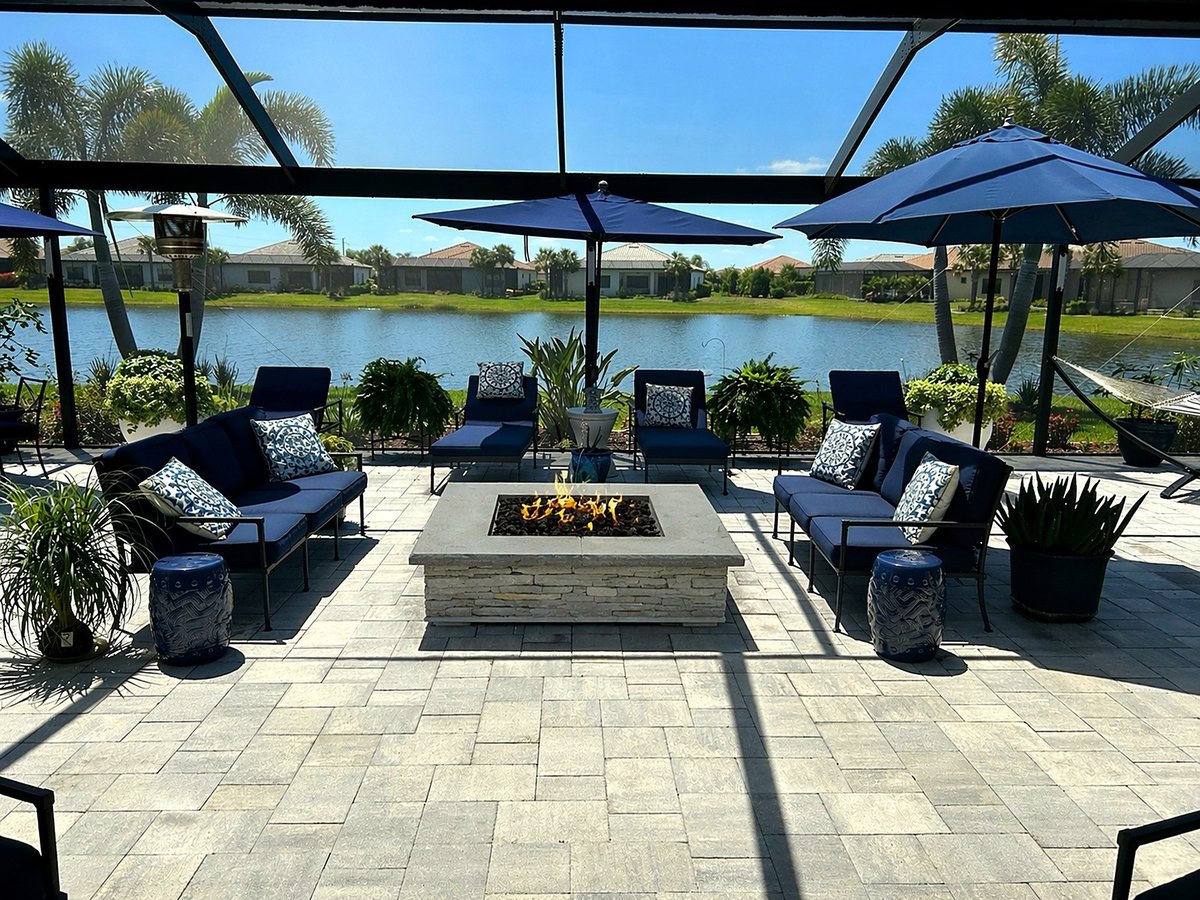 Lakewood Ranch paver patio with a stone-faced gas fire pit and seating inside a lakeside screened enclosure.