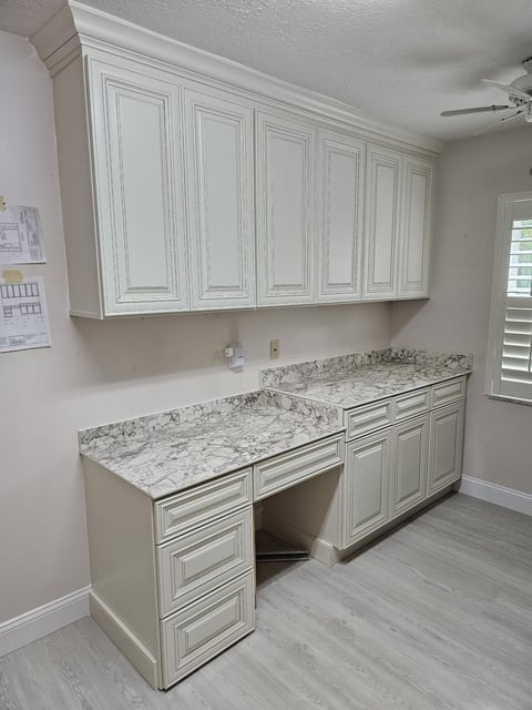 Light raised-panel laundry cabinetry with gray-veined countertops and built-in work surface.