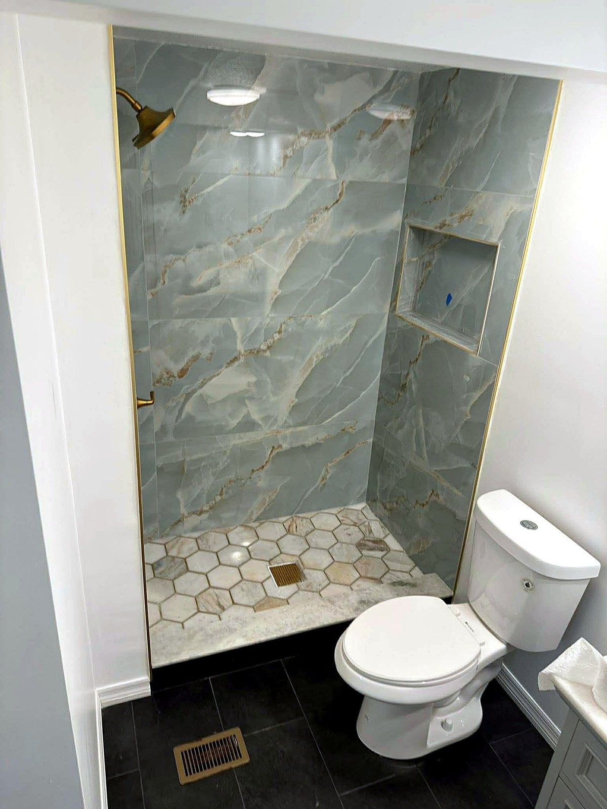 Bradenton shower with marble-look wall tile, recessed niche, hexagonal floor tile and gold-tone trim.