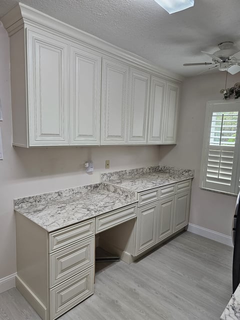 Laundry room cabinetry with raised-panel doors, crown molding and gray-veined work surfaces.