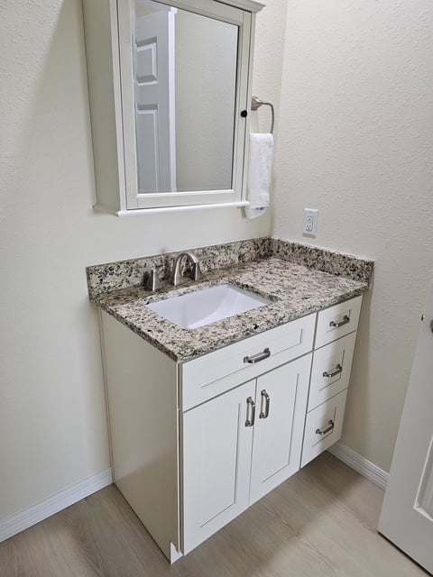 Single bathroom vanity with white cabinetry, undermount sink, mirrored storage and speckled countertop.
