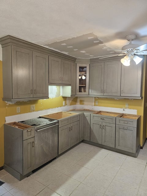 Gray shaker kitchen cabinets surrounding a corner workspace and dishwasher during remodeling.