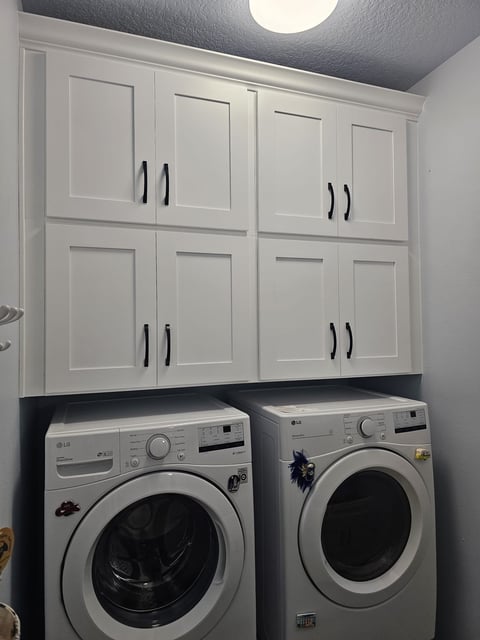 Custom white laundry cabinetry above washer and dryer.