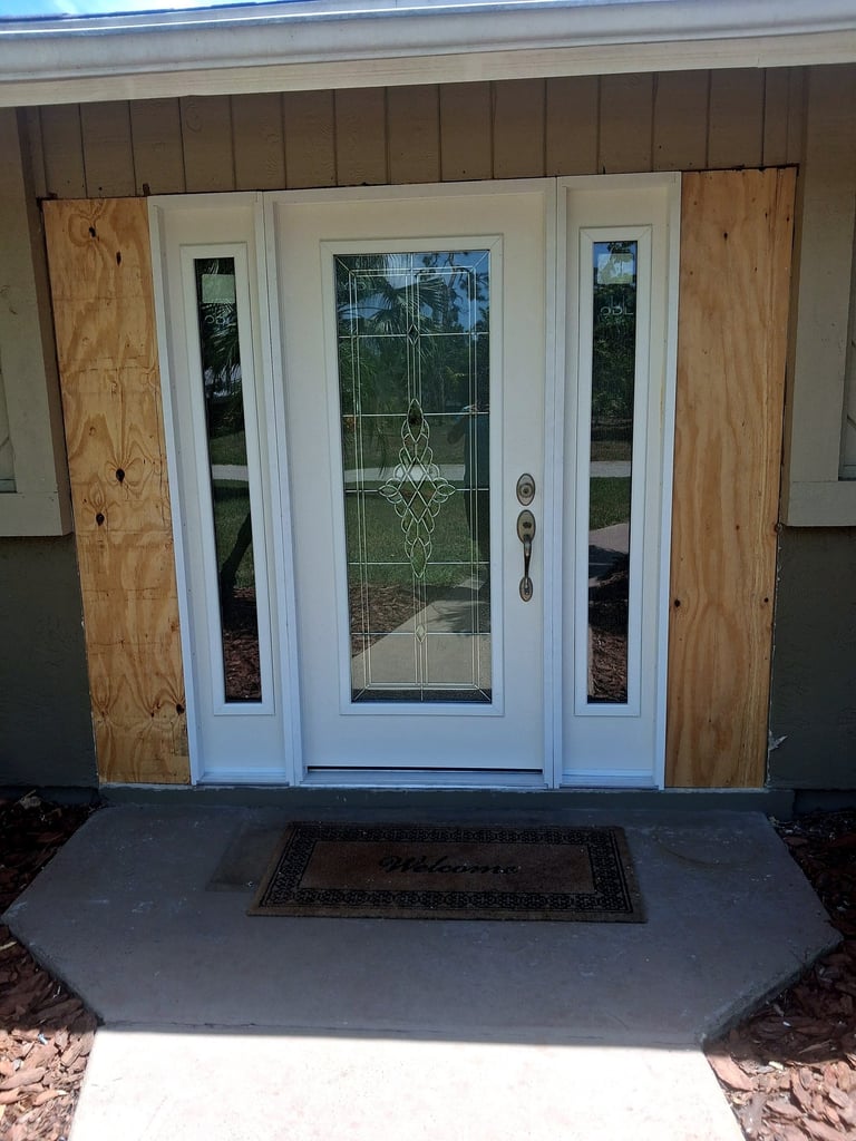 White decorative-glass entry door and sidelights during installation, with exposed surrounding sheathing.