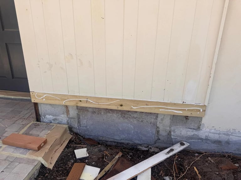 Before / preparation: Entry wall base with exposed masonry and an unfinished horizontal trim board beside the paver step.