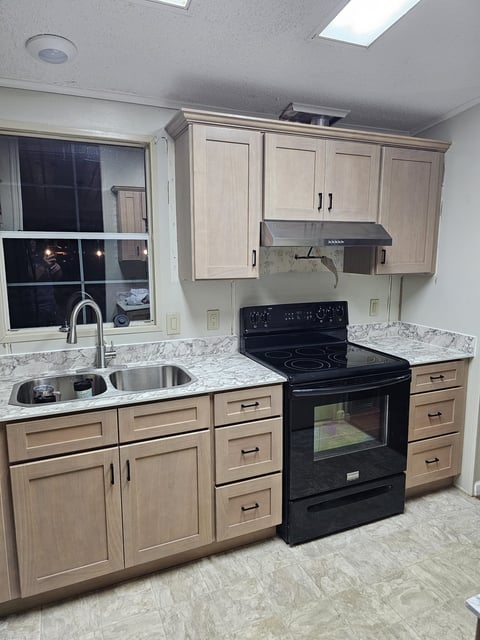 Light kitchen cabinetry with double-basin sink, black electric range and stainless steel range hood.