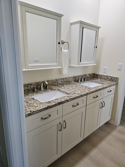 White double bathroom vanity with two sinks, speckled countertop and mirrored medicine cabinets.