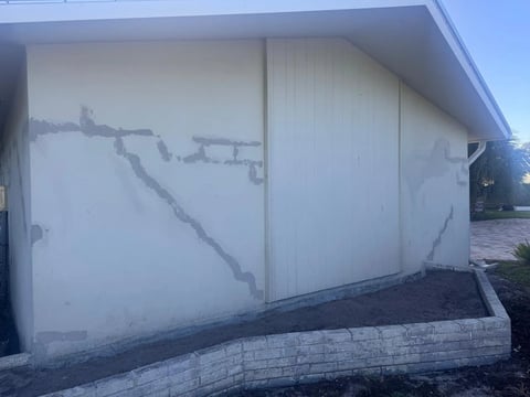 Before / preparation: Gable-end exterior wall with visible gray patch lines above a low landscape retaining wall.