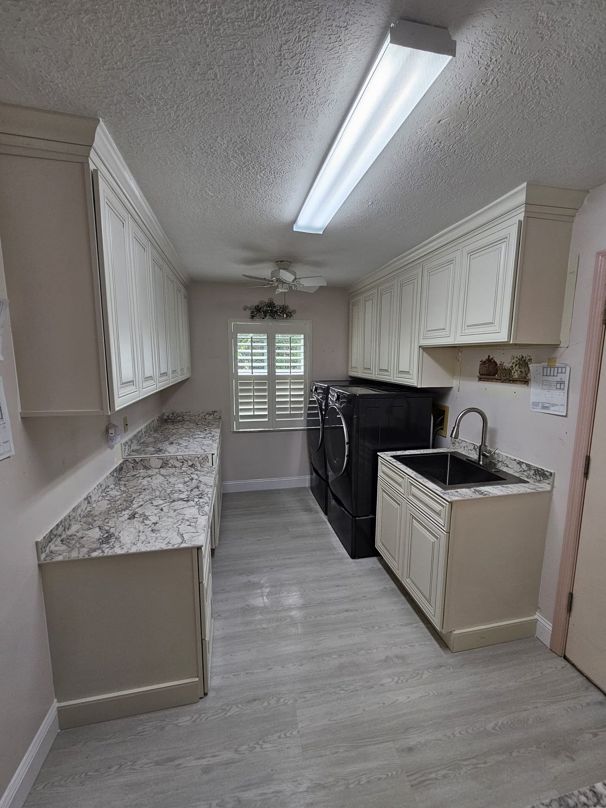 Laundry room remodel with light raised-panel cabinetry, a washer and dryer, a utility sink and gray-veined countertops.
