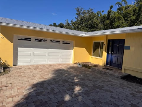After: Yellow garage and entry elevation with a white garage door and dark blue front door.