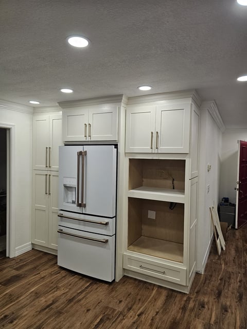 White tall kitchen cabinetry surrounding a refrigerator with adjacent built-in storage openings.