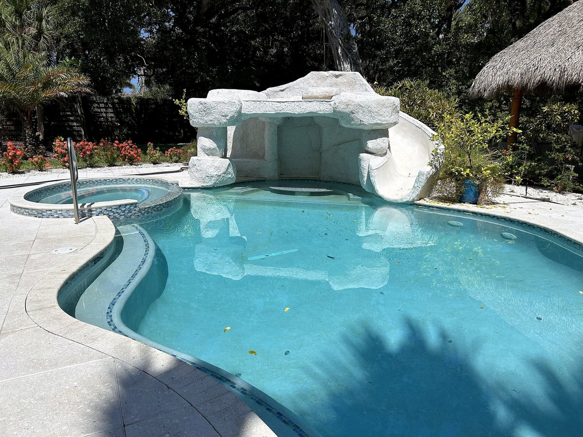 Siesta Key swimming pool with a rock-style grotto, integrated slide, round spa and light-colored pool decking.