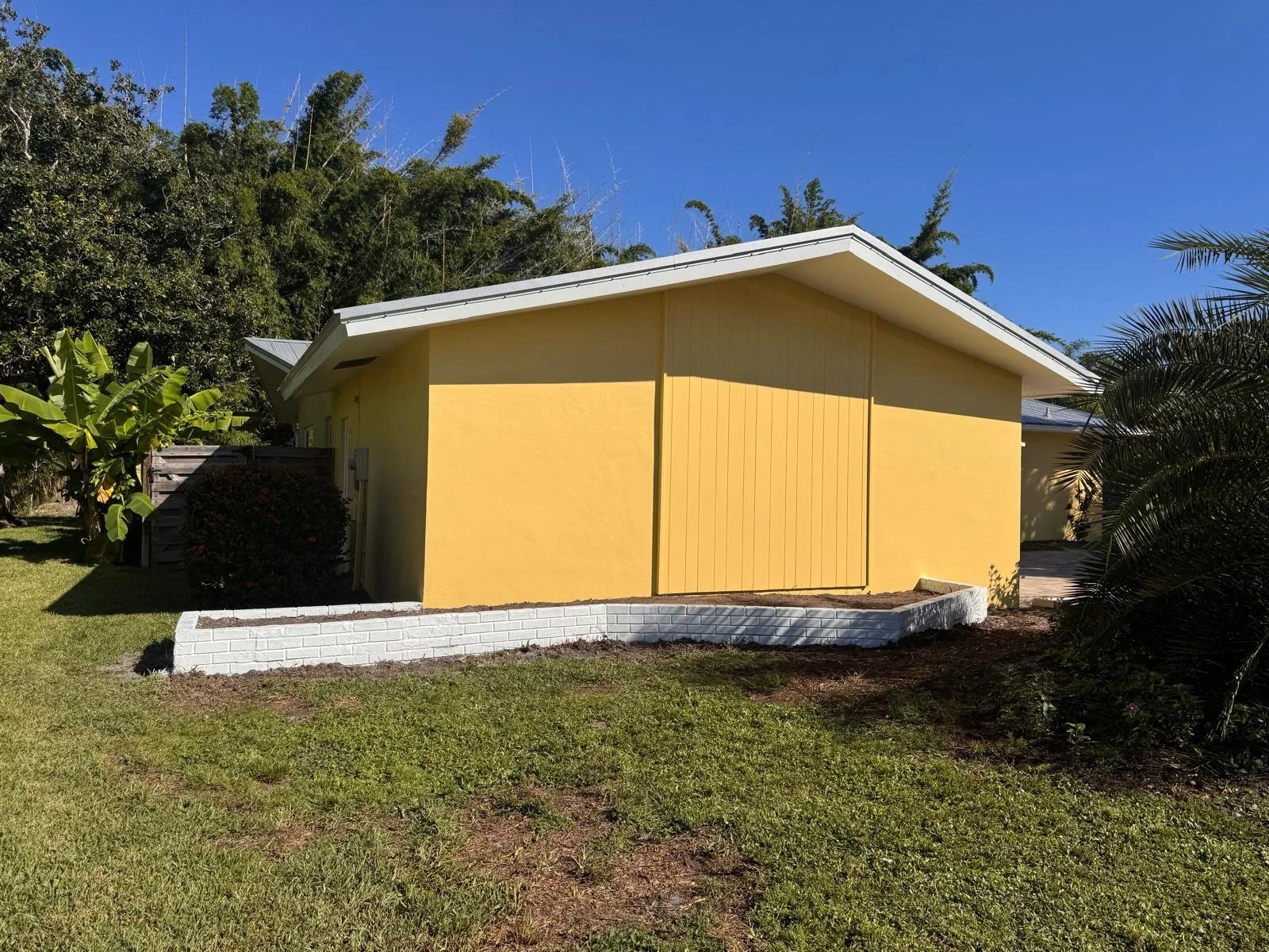 After: Completed yellow gable-end wall above the low retaining wall and lawn.