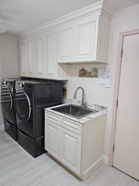 Laundry room with dark washer and dryer, utility sink and surrounding light cabinetry.