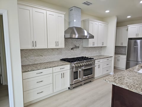 White kitchen cabinetry surrounding stainless steel range and hood with patterned backsplash.