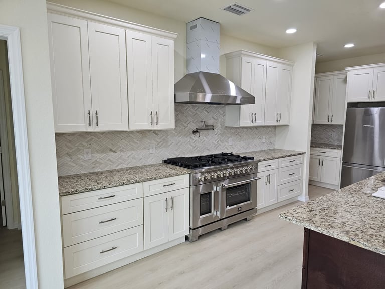 White kitchen cabinetry surrounding stainless steel range and hood with patterned backsplash.