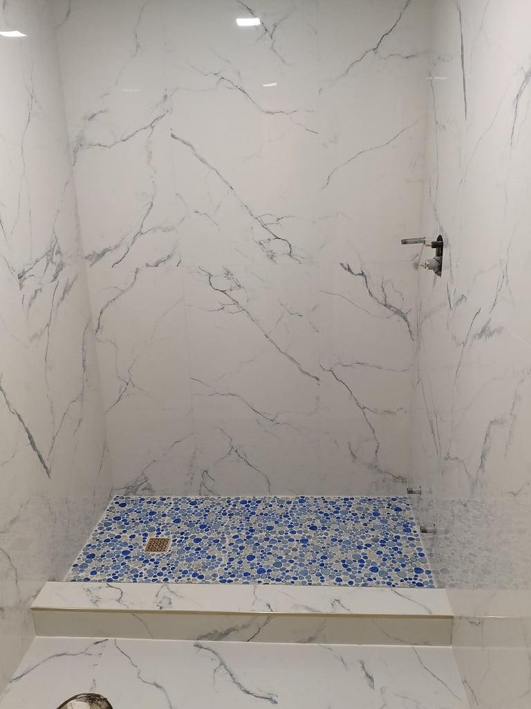 Venice shower remodel in progress with marble-look wall tile and blue-and-gray mosaic shower floor.