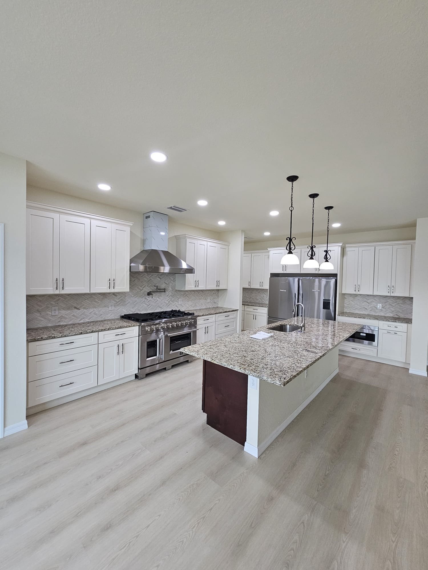 Kitchen renovation with white shaker cabinets, large center island, stainless steel appliances and light speckled countertops.