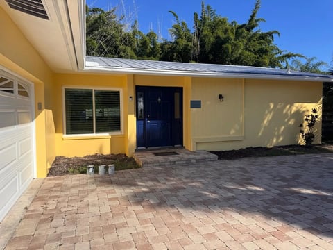After: Angled courtyard view of the finished yellow facade, dark blue door and white-trimmed window.