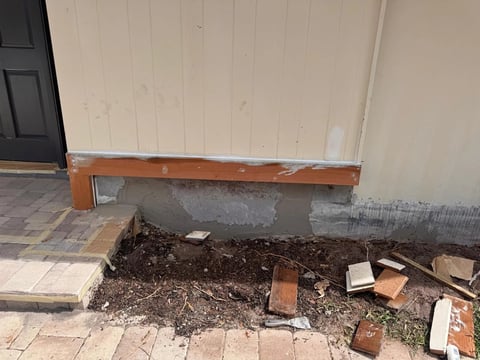 Before / preparation: Wider entry-wall view showing unfinished wood trim, gray wall-base patches and the adjacent planting bed.