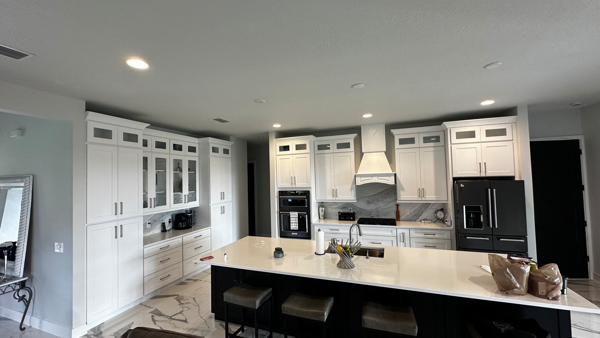 After photo of a Nokomis kitchen remodel with white shaker cabinets, a contrasting dark island, glass-front display cabinets and marble-look flooring