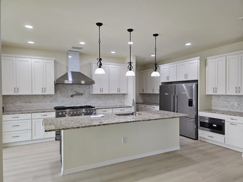 White kitchen cabinetry with large island, stainless steel range, refrigerator and pendant lighting.