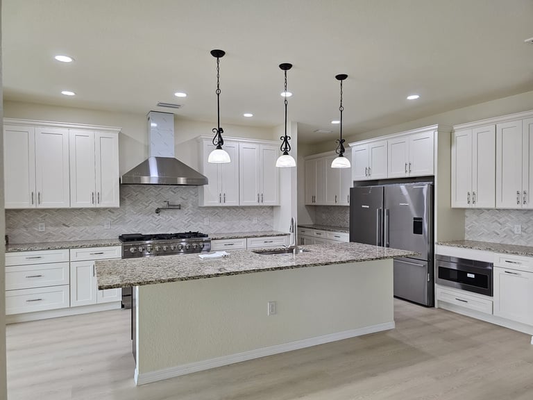 White kitchen cabinetry with large island, stainless steel range, refrigerator and pendant lighting.